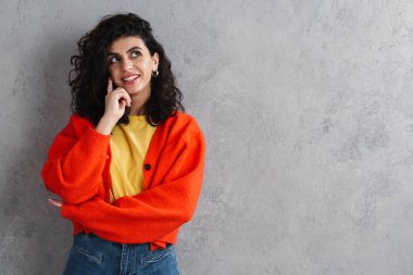 Mutlu güzel esmer kız gülümsüyor ve yukarı bakıyor gri duvarın üzerinde.