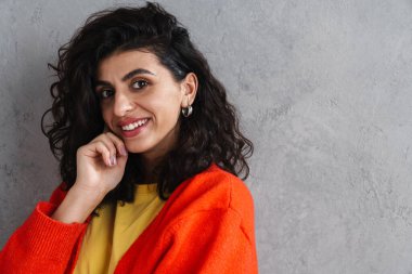 Gri duvarın üzerinden izole edilmiş kameraya poz veren ve gülümseyen güzel esmer kız.