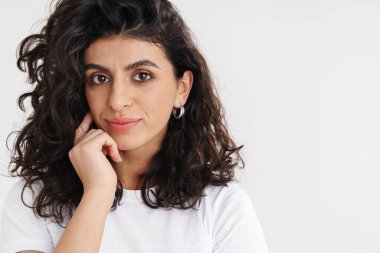 Güzel esmer kız beyaz arka planda yalnız poz veriyor ve kameraya bakıyor.