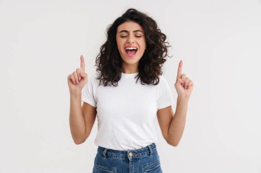 Neşeli, güzel esmer kız çığlık atıyor ve beyaz arka planda izole bir şekilde parmaklarını yukarı kaldırıyor.
