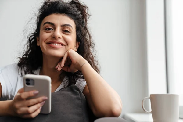 Jovem Morena Feliz Usando Telefone Celular Enquanto Senta Sofá Casa — Fotografia de Stock