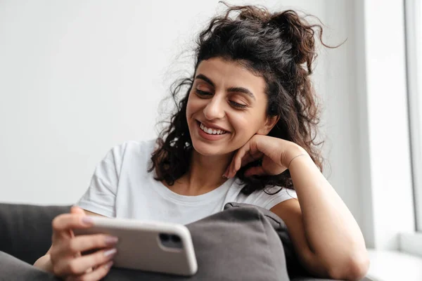 Jovem Morena Feliz Usando Telefone Celular Enquanto Senta Sofá Casa — Fotografia de Stock