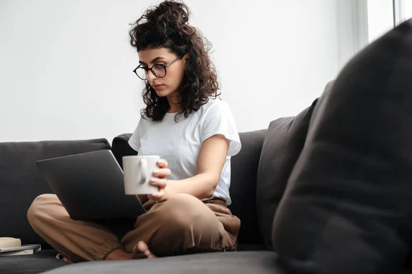 Seriöse Brünette Junge Frau Arbeitet Mit Laptop Und Trinkt Kaffee — Stockfoto