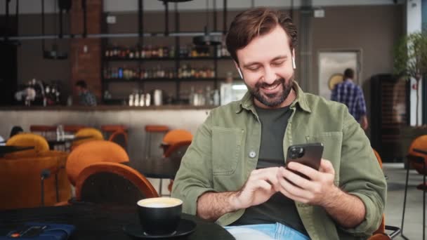 Hombre Sonriente Está Usando Teléfono Inteligente Mientras Bebe Café Sentado — Vídeo de stock