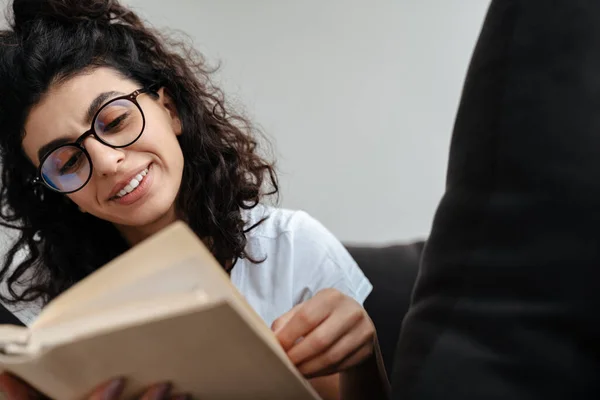 Mujer Joven Sonriente Gafas Lectura Libro Mientras Descansa Sofá Casa — Foto de Stock