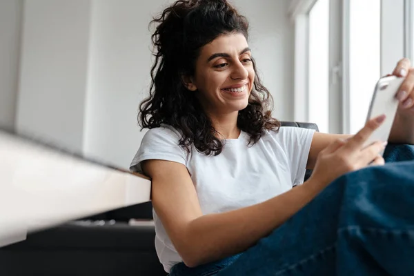 Jovem Morena Feliz Usando Telefone Celular Enquanto Está Sentado Casa — Fotografia de Stock