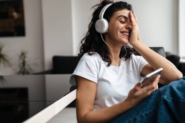 Evde otururken kulaklık takan neşeli esmer kadın.