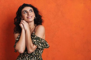 Mutlu güzel esmer kız gülümsüyor ve yukarı bakıyor turuncu arka planda.