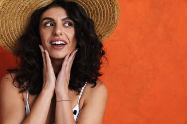 Mayo giymiş neşeli güzel bir kadın turuncu arka planda tek başına bakarken gülümsüyor.