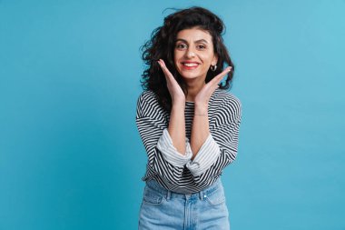 Çekici gülümseyen genç bir kadın mavi arka planda yalnız poz veriyor, kameraya bakıyor.