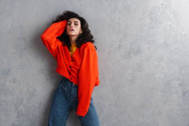 Gri arka planda yalnız poz veren kendine güvenen çekici genç bir kadın.