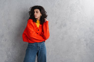 Gri arka planda yalnız poz veren kendine güvenen çekici genç bir kadın.