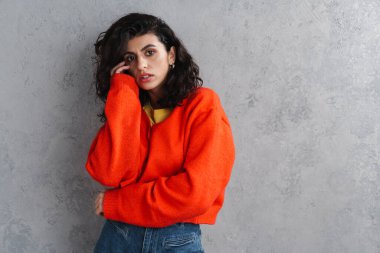 Gri arka planda yalnız poz veren kendine güvenen çekici genç bir kadın.