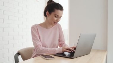 Pembe tişörtlü konsantre bir kadının bir kafede otururken laptopta bir şey ararken yan görüntüsü.