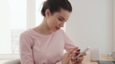 Pembe tişörtlü, kafede otururken telefonda bir şeyler yazan pozitif kadının yan görüntüsü.