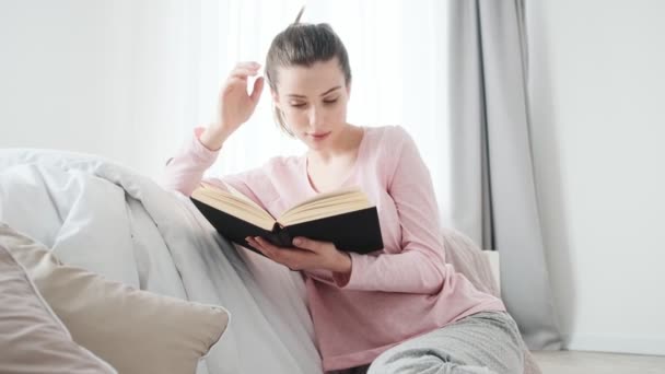 Uma Menina Sorrindo Lendo Livro Suas Mãos Enquanto Sentada Sofá — Vídeo de Stock