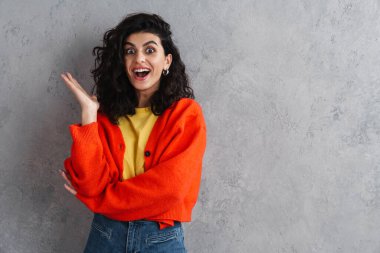 Gri duvardan izole edilmiş kameraya bağıran ve el kol hareketi yapan güzel esmer kız.