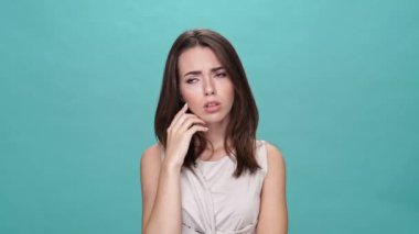 Tişörtlü üzgün esmer kadın, turkuaz arka planda kameraya bakarken dinlemek istemiyor.