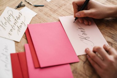 Kapalı bir masada sevgililer günü kartı üzerinde çalışırken kaligraf kız yazı yazıyor.
