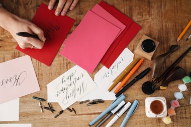 Kapalı bir masada sevgililer günü kartı üzerinde çalışırken kaligraf kız yazı yazıyor.