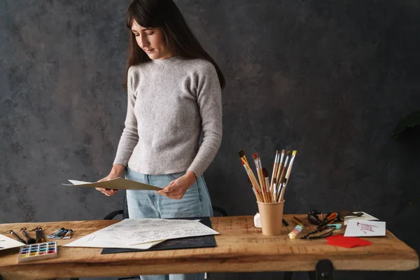 Odaklanmış güzel kaligraf kız kapalı bir masada çizimlerle çalışıyor.