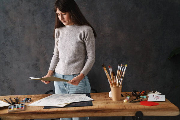 Сосредоточена на красивой девушке-каллиграфе, работающей с эскизами за столом в помещении