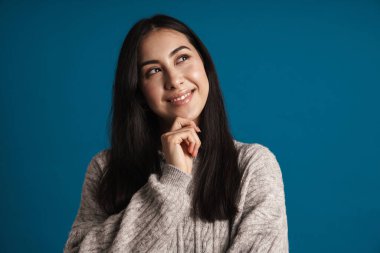 Mutlu, güzel Asyalı kız gülümsüyor ve mavi arka planda tek başına bir kenara bakıyor.