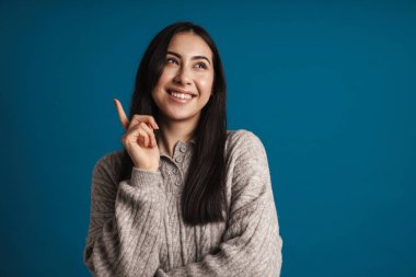 Mutlu, güzel Asyalı kız gülümsüyor ve mavi arka planda tek başına parmağını yukarı kaldırıyor.