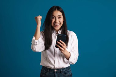 Mavi arka plan üzerinde izole akıllı telefon kullanarak kazanan jest yapan Asyalı kız çıktı