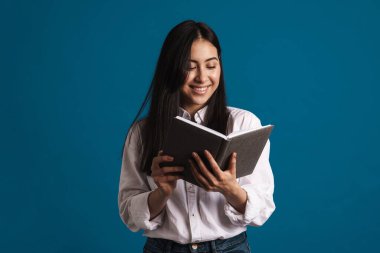 Mutlu, güzel Asyalı kız gülümserken mavi arka planda izole edilmiş planlamacıyla poz veriyor.