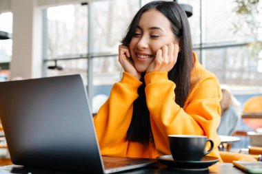 Kafede otururken bilgisayarla çalışan gülümseyen Asyalı kadın.