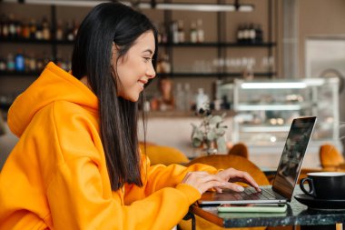 Kafede otururken bilgisayarla çalışan gülümseyen Asyalı kadın.