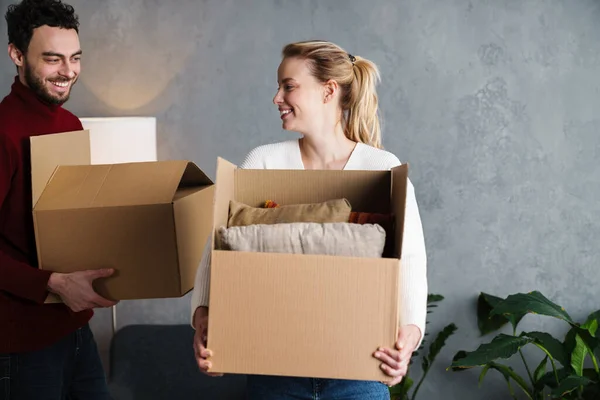 箱に囲まれた新しい家の中で一緒に動く笑顔のカップルの肖像画 箱を運ぶ — ストック写真