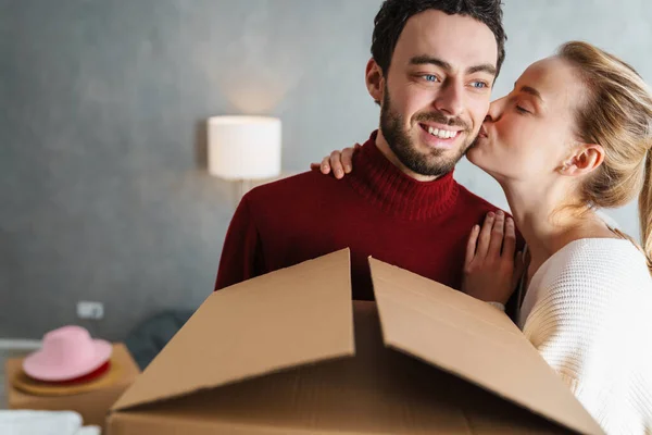 一对笑容满面的夫妻在一幢新房子里抱着盒子接吻的画像 — 图库照片