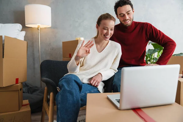 Leende Par Med Laptop Sittande Golvet Nytt Hus Viftande Händer — Stockfoto