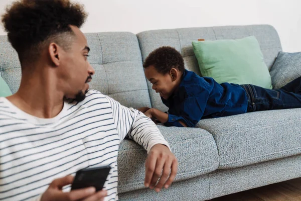 Afroamericanos Padre Hijo Usando Teléfono Móvil Mientras Descansan Casa —  Fotos de Stock