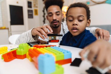 Odaklanmış Afrikalı Amerikalı çocuk evde babasıyla oynuyor.