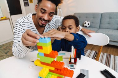 Mutlu Afrikalı Amerikalı çocuk evde gülümseyen babasıyla oynuyor.