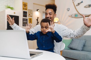 Mutlu Afro-Amerikan baba ve oğlu evde dizüstü bilgisayar kullanırken dalga geçiyor.