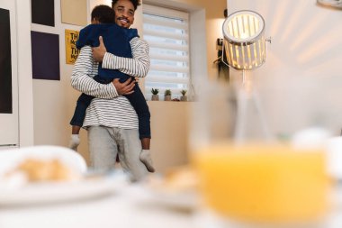 Genç Afrikalı baba, mutfakta durup kahvaltı ederken oğlunu kucağına aldı.