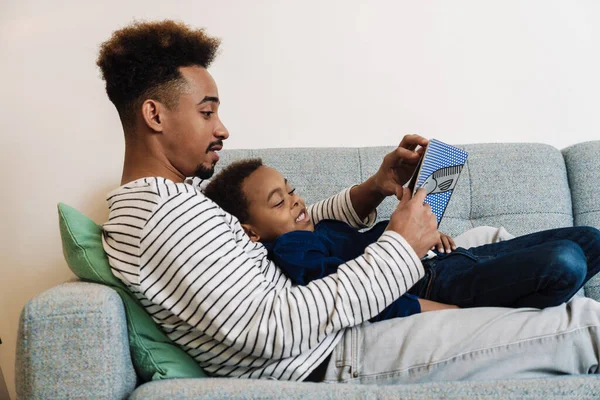 Enfocado Afroamericano Padre Hijo Leyendo Libro Mientras Descansa Sofá Casa —  Fotos de Stock