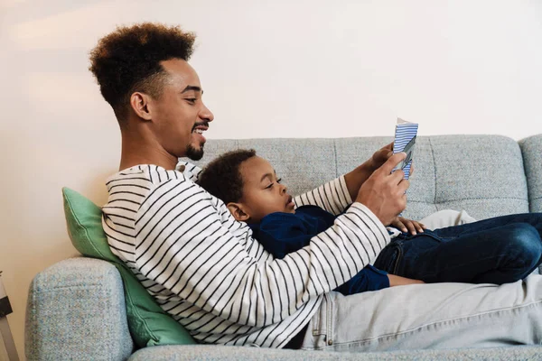 Feliz Afroamericano Padre Hijo Leyendo Libro Mientras Descansa Sofá Casa —  Fotos de Stock