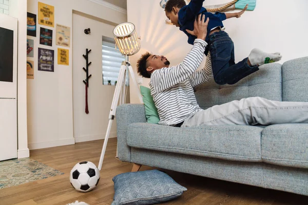 Mutlu Afro-Amerikan baba ve oğlu evdeki kanepede oynayıp eğleniyor.