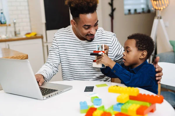 Mutlu Afro-Amerikan baba ve oğlu evde oynarken laptop kullanıyor.