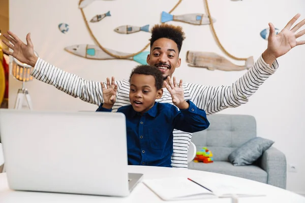 Mutlu Afro-Amerikan baba ve oğlu evde dizüstü bilgisayar kullanırken dalga geçiyor.
