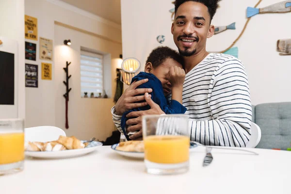 African american father and son hugging while having breakfast at home