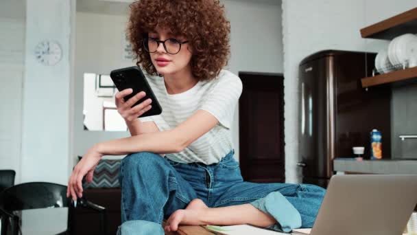 Uma Menina Cabelos Encaracolados Rindo Óculos Folheando Algo Telefone Casa — Vídeo de Stock