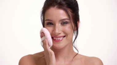 Pozitif yarı çıplak bir kadının yakın plan görüntüsü stüdyodaki beyaz duvarın üzerinde duran yumuşak bir süngeri tutuyor.