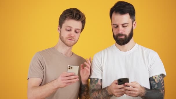 Два Улыбающихся Парня Используют Свои Смартфоны Стоящие Изолированно Над Жёлтой — стоковое видео