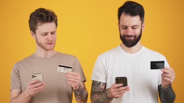 Dois Caras Sorridentes Estão Usando Seus Smartphones Enquanto Segurando Cartão — Vídeo de Stock